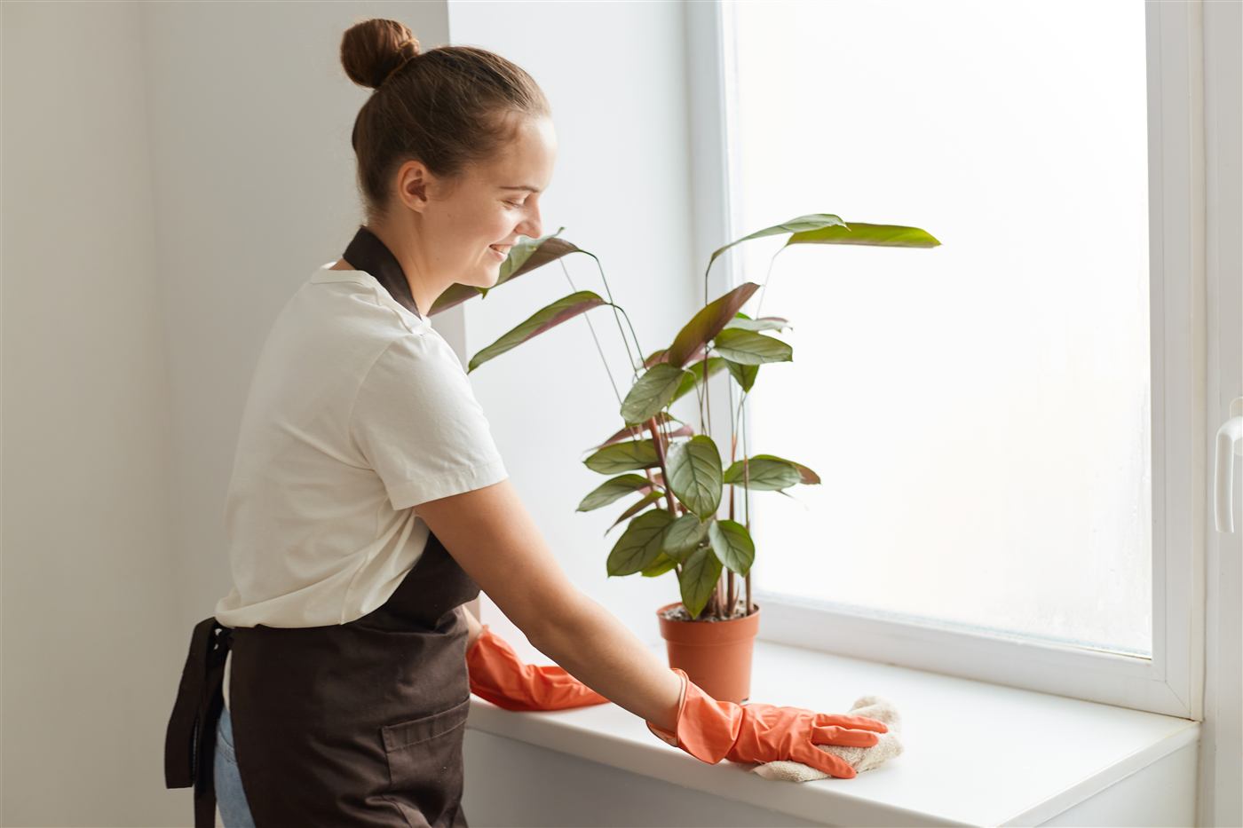 Cleaner in an apron dusting a windowsill and radiator during an after builders clean in Coatbridge
